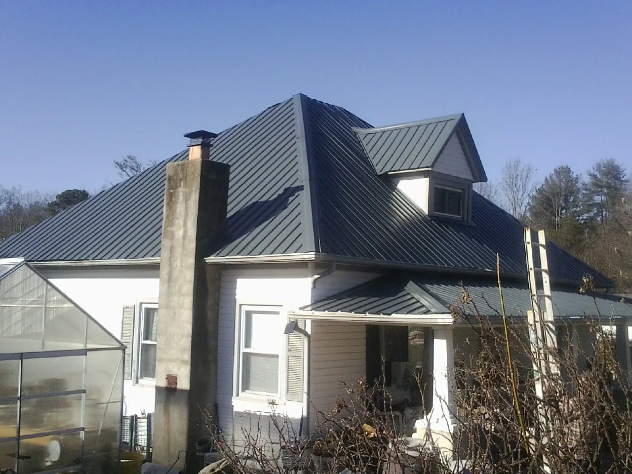 Dark blue standing seam metal roof on a white farmhouse with dormer — Slate & Tile Roof Repair by Roofing Brothers in Kansas