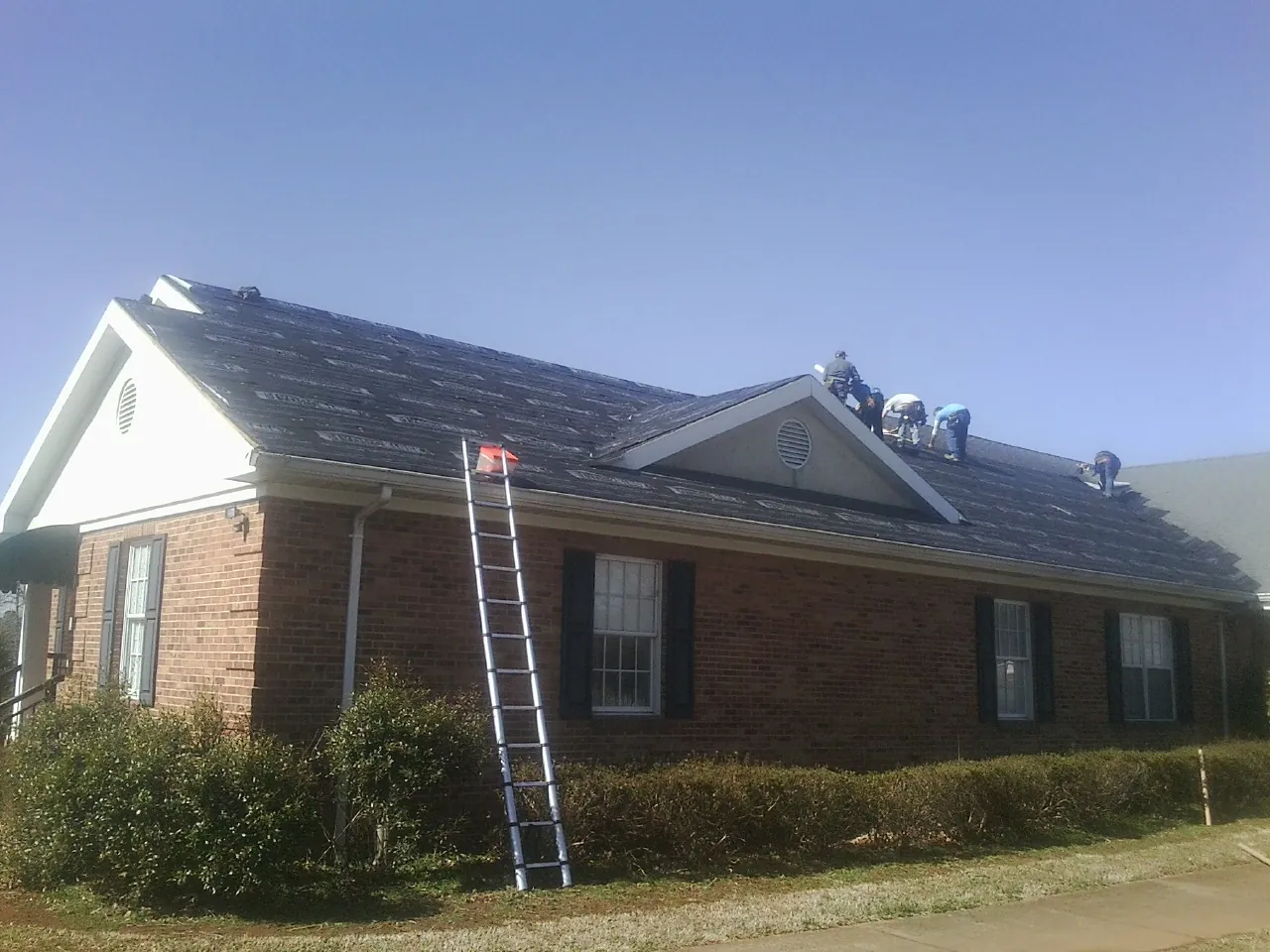Crew tearing shingles off a brick ranch roof with a ladder set — Metal Roof Repair work by our crew in Kansas
