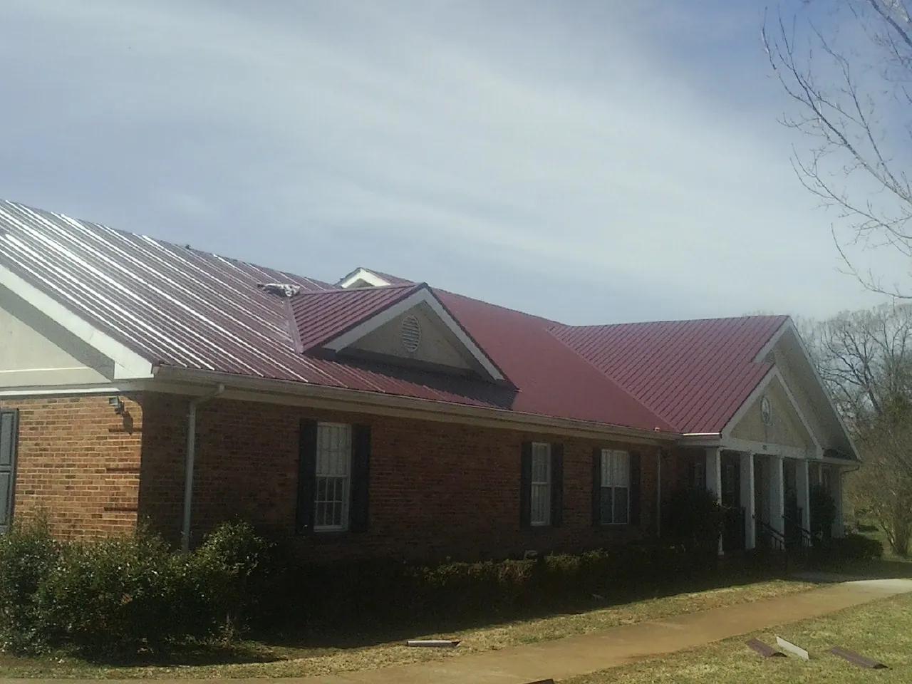Red metal roof with gabled entries on a long brick building, from a Hail Damage Roof Repair job in Kansas