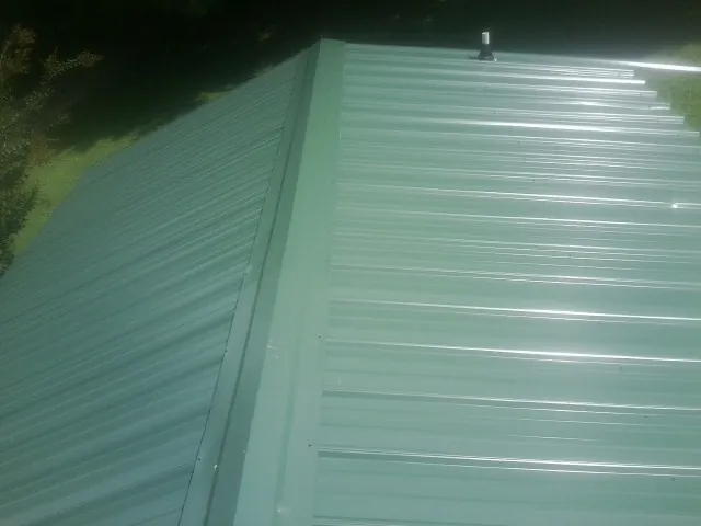 New green metal panels meeting at the ridge of a roof — Flat Roof Repair work by our crew in Kansas