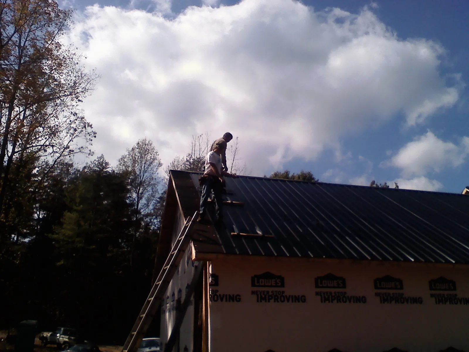 Roofer fastening dark metal panels high against a cloudy sky, from a Roof Inspection job in Kansas