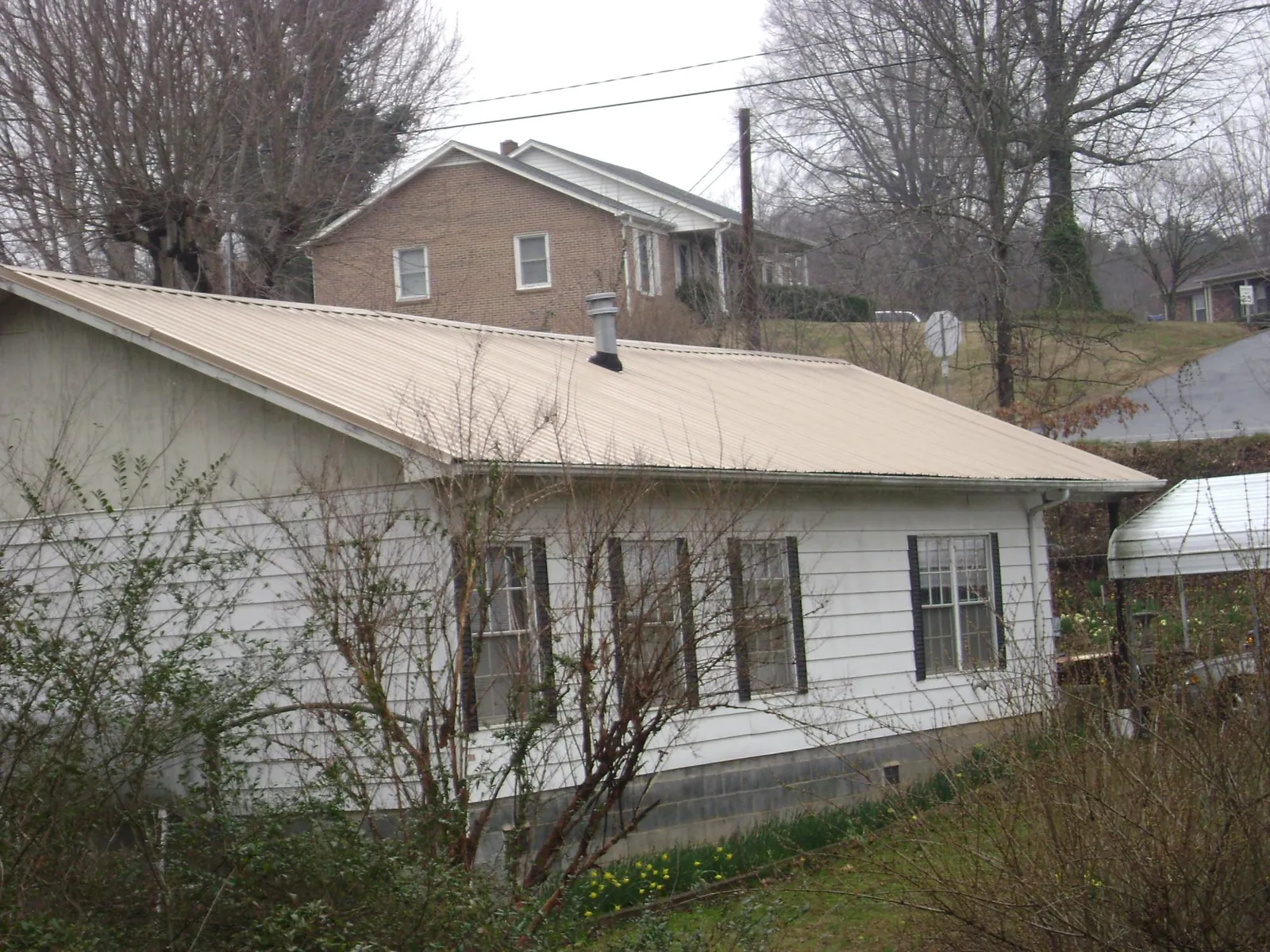 Tan metal roof on a white sided house set into a hillside — Commercial Roofing by Roofing Brothers in Kansas
